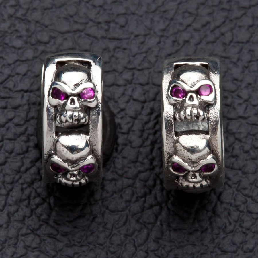 Paire de boucles d'oreilles créoles huggie en argent sterling .925 avec crânes, chaque bande de 6 mm sculptée d'une rangée de crânes aux yeux en zircone cubique rouge.