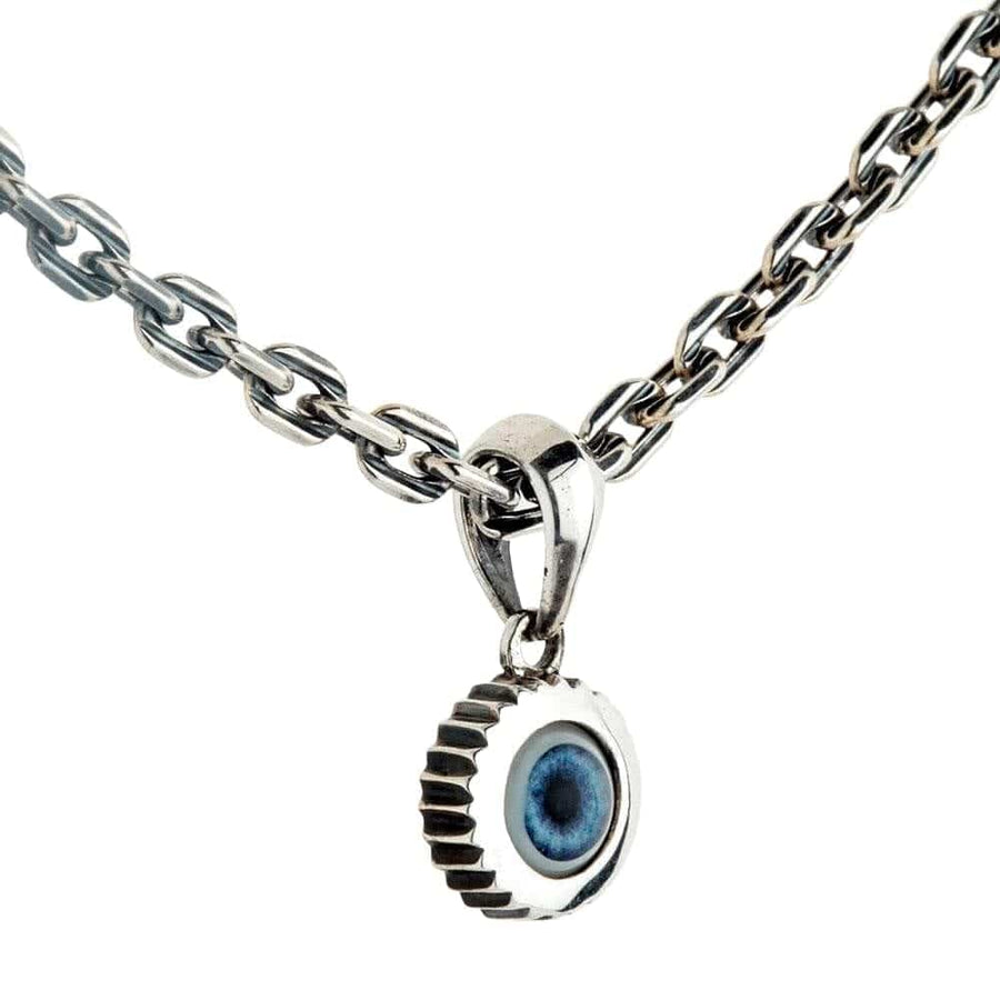 Un pequeño colgante de ojo malo en plata esterlina con un bisel único de estilo engranaje, mostrado en una cadena de plata.