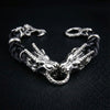 Sterling silver dual dragon head bracelet with black braided leather band and dragon claw clasp on black leather background