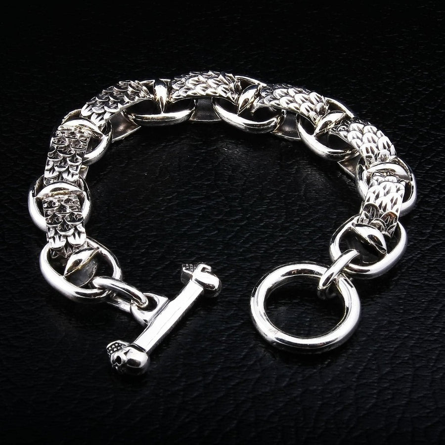 Sterling silver dragon scale bracelet with skull toggle clasp displayed on black leather background