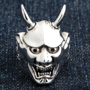 A front view of the large sterling silver Oni mask ring resting on a dark denim background.