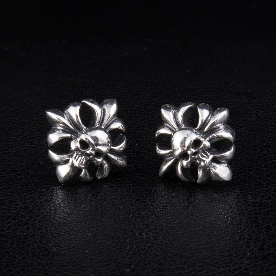 Une paire de boucles d'oreilles tête de mort en argent sterling avec des détails gothiques en filigrane, sur fond noir.