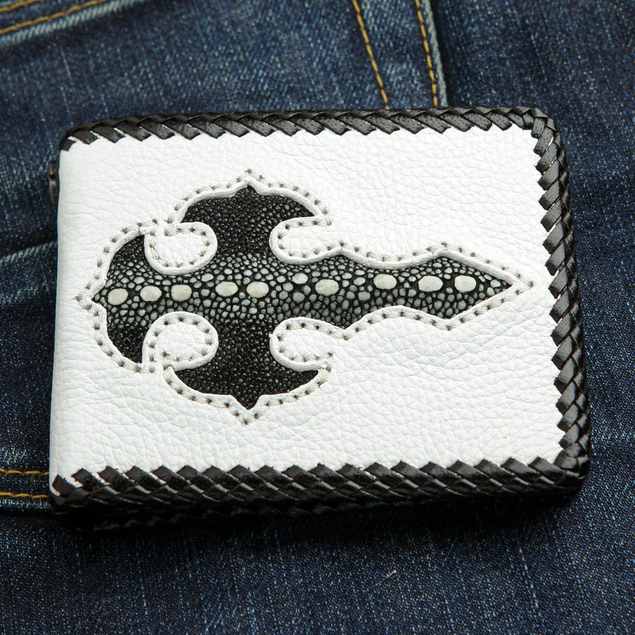 Le portefeuille de motard en cuir blanc fait à la main avec une incrustation de croix gothique en galuchat noir, posé sur un jean bleu.