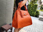 A woman wearing the large, genuine orange ostrich leather tote bag, showing its size and style.