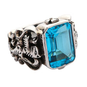 Angled view of the heraldic ring featuring a large emerald-cut blue topaz and lion carving.
