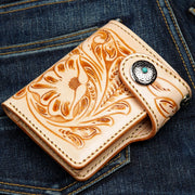 A handcrafted, hand-tooled western leather wallet with floral carving, shown on denim.