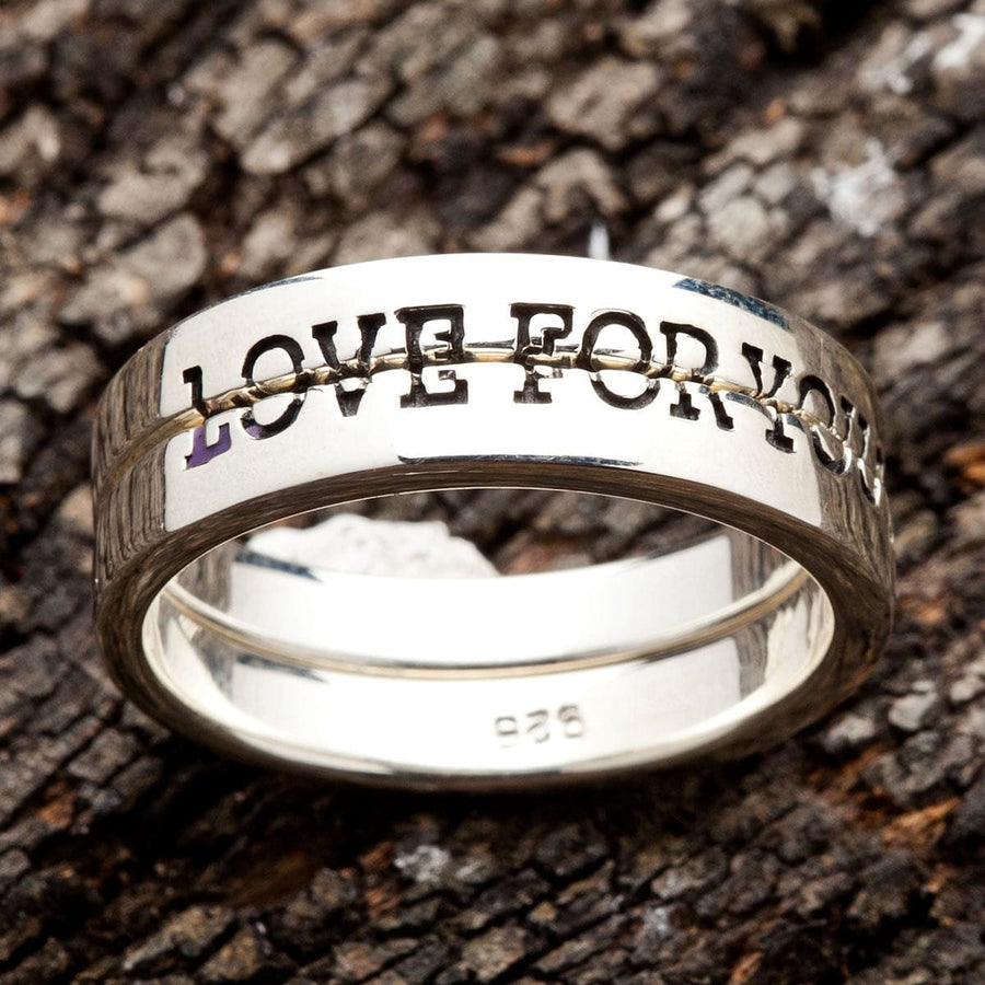 Primer plano de los dos anillos de promesa apilados sobre corteza, con letras oscurecidas alrededor del exterior
