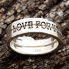Close-up of the two promise bands stacked on bark, darkened lettering running around the outer ring