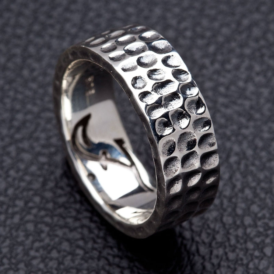 Un anello a banda in argento battuto per uomo con un finitura testurata unica, ruvida e sapientemente realizzata, mostrato su una superficie in pelle.