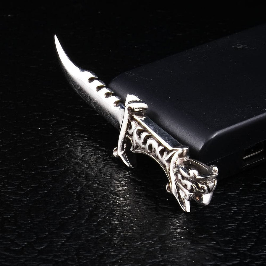Silver dagger pendant on a black phone, showing the upswept curved blade, notched spine, and openwork scroll hilt.