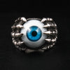 Een sterling zilveren klauwring met oogbol, met een realistisch blauw oog vastgehouden door een skelethand, getoond op een zwarte achtergrond.